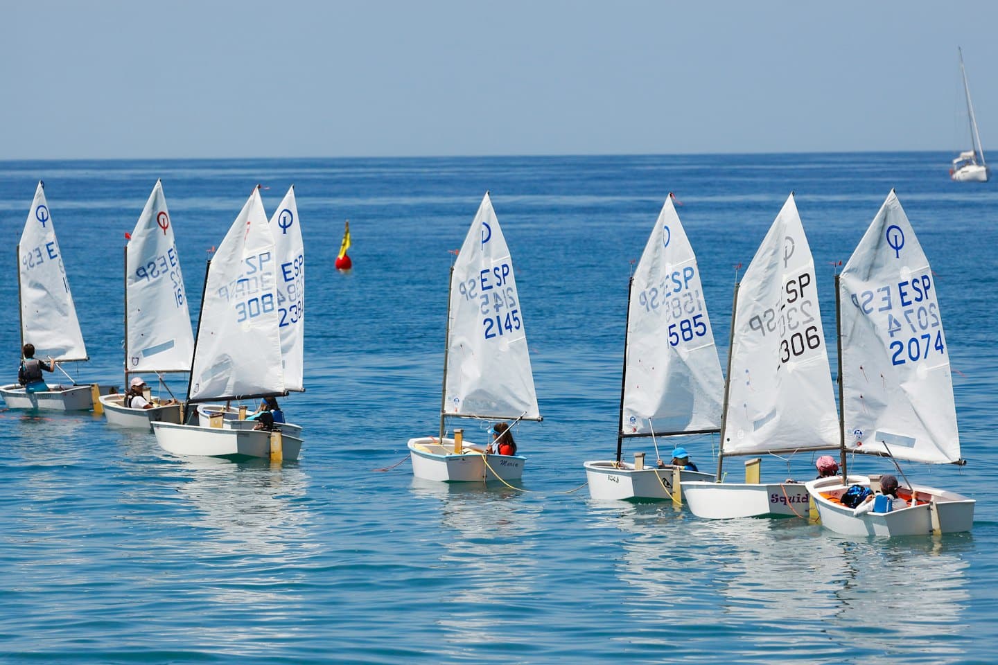 Kindersegeln mit Optimisten auf einem ruhigen blauen See.