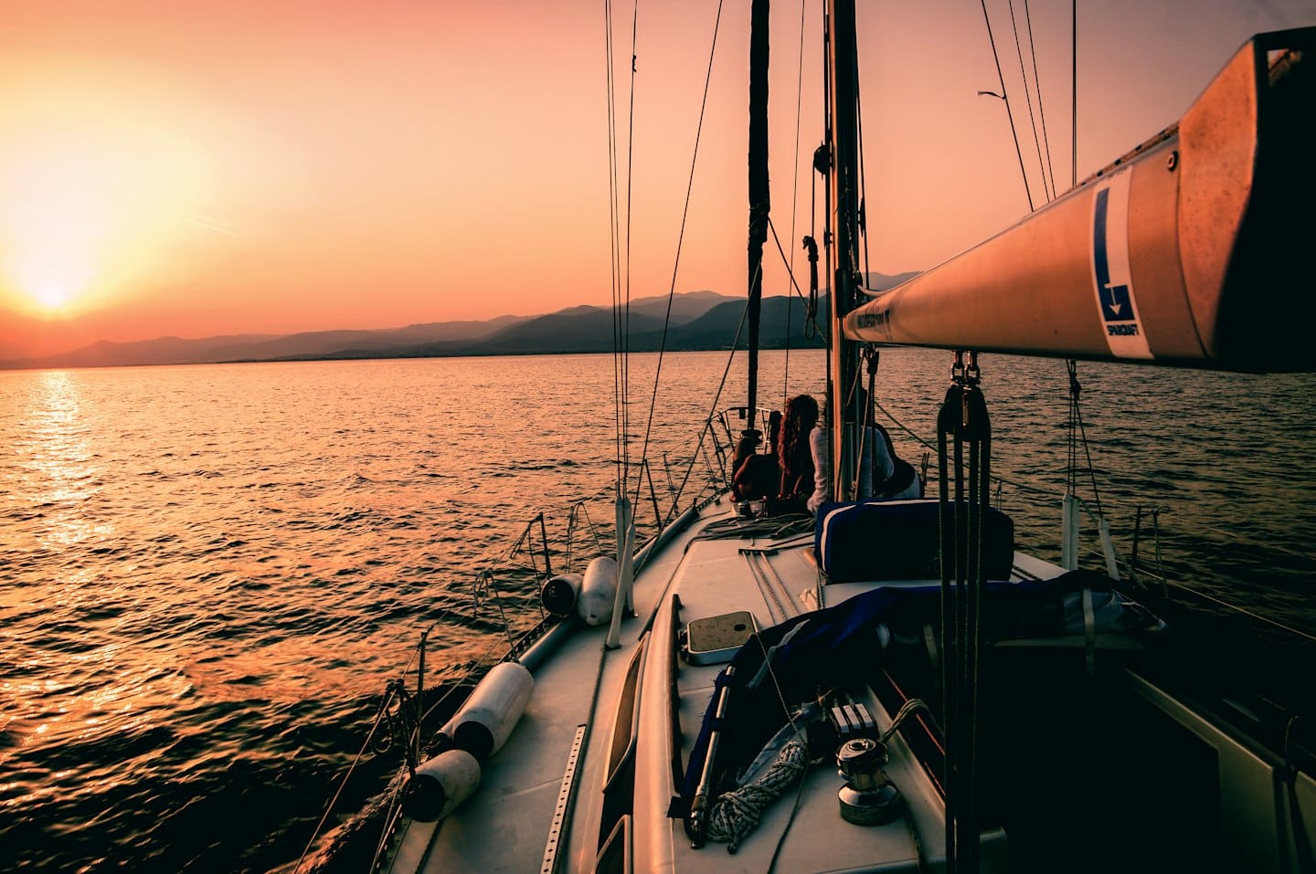 Menschen entspannen sich auf einem Segelbootdeck bei Sonnenuntergang.