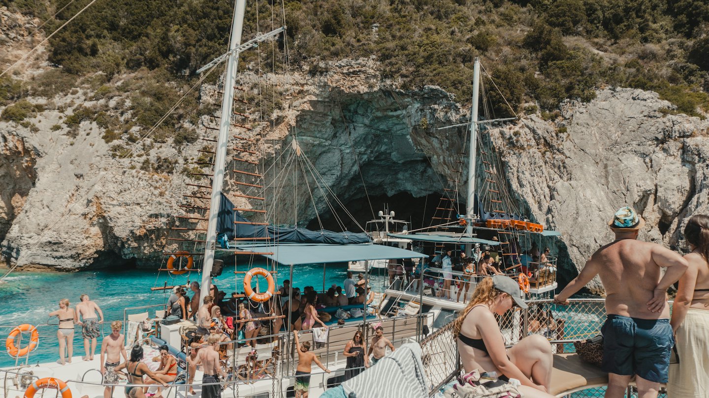 Menschen schwimmen und entspannen auf Segelbooten in der Nähe einer großen Küstenhöhle.