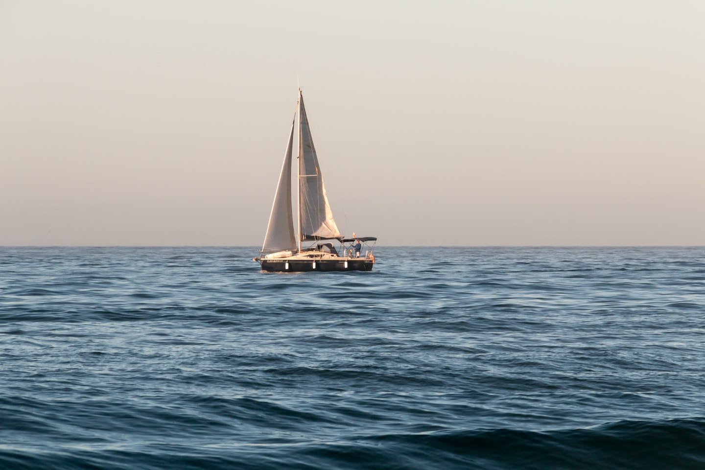 Ein Segelboot mit weißen Segeln gleitet auf ruhigem Meer.