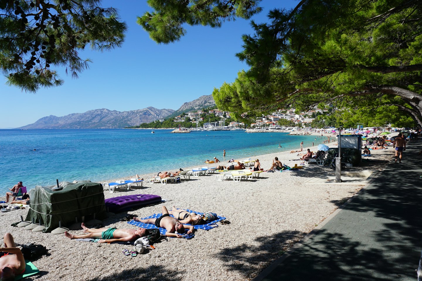 Menschen schwimmen und entspannen sich an einem Kieselstrand in einer Küstenstadt.