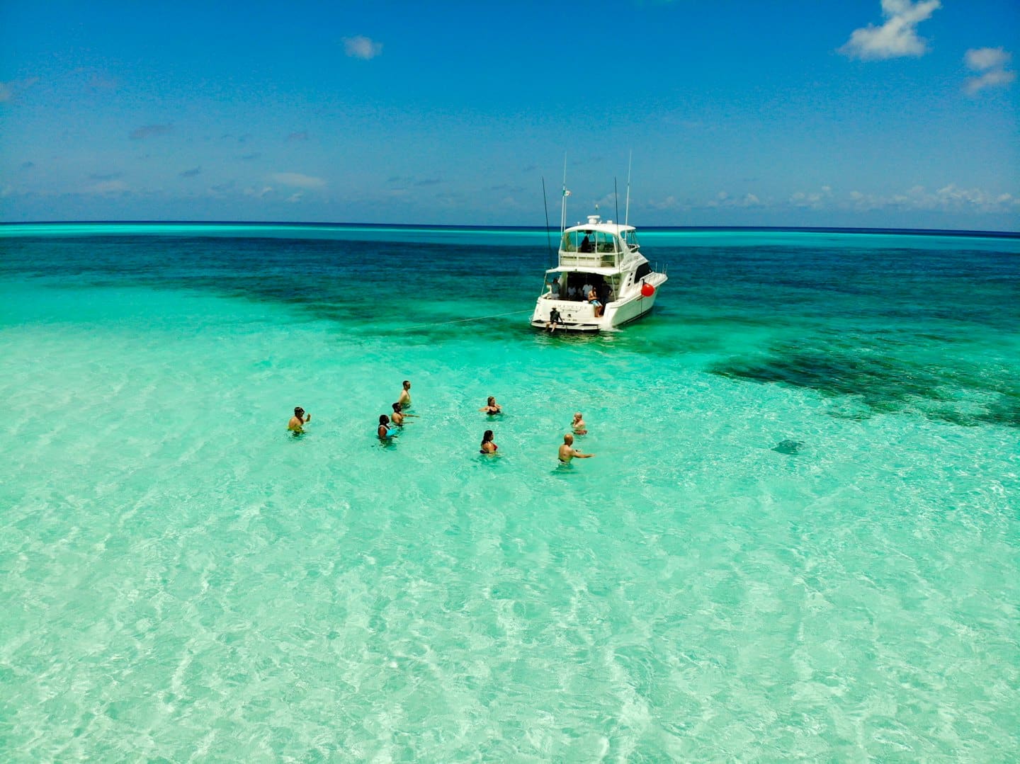 Menschen schwimmen und stehen in der Nähe einer Yacht in klarem türkisfarbenem Wasser.