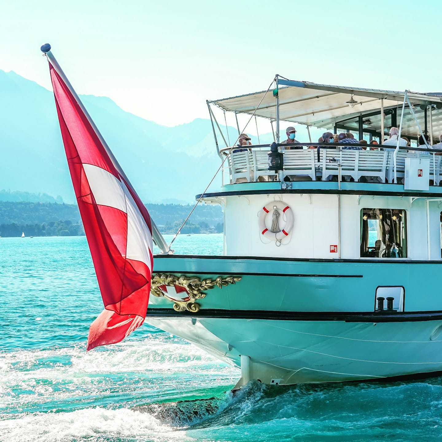 Eine Passagierfähre mit Touristen fährt an Bergen auf türkisfarbenem Wasser vorbei.