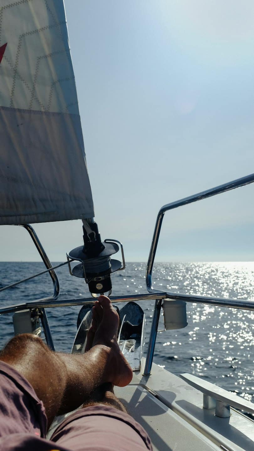 Eine Person entspannt sich auf dem Deck eines Segelboots und legt die Füße auf die Reling.