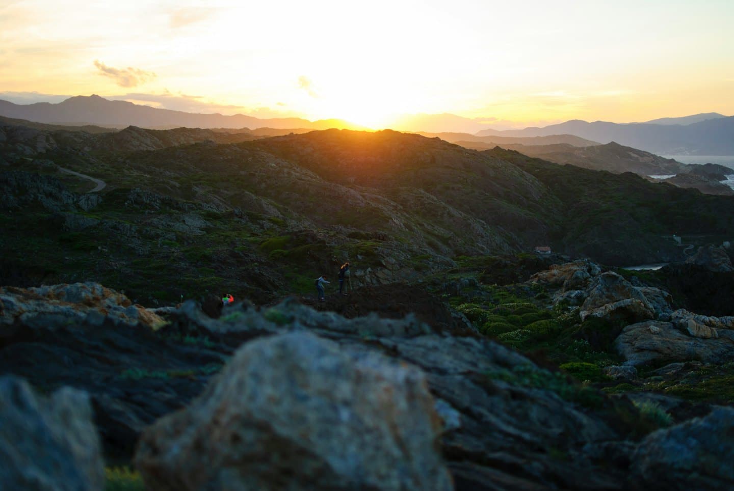 Wanderer auf felsigen Küstenhügeln bei Sonnenuntergang.